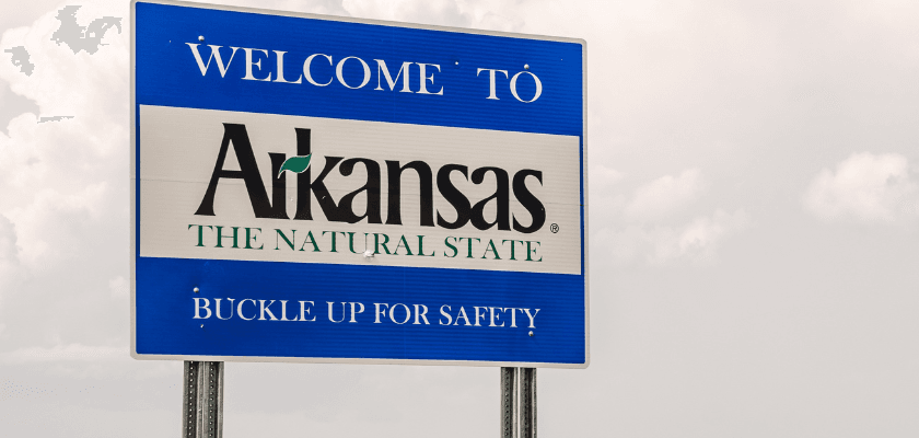 A welcome sign for Arkansas featuring the phrase "The Natural State" and a safety reminder to buckle up.
