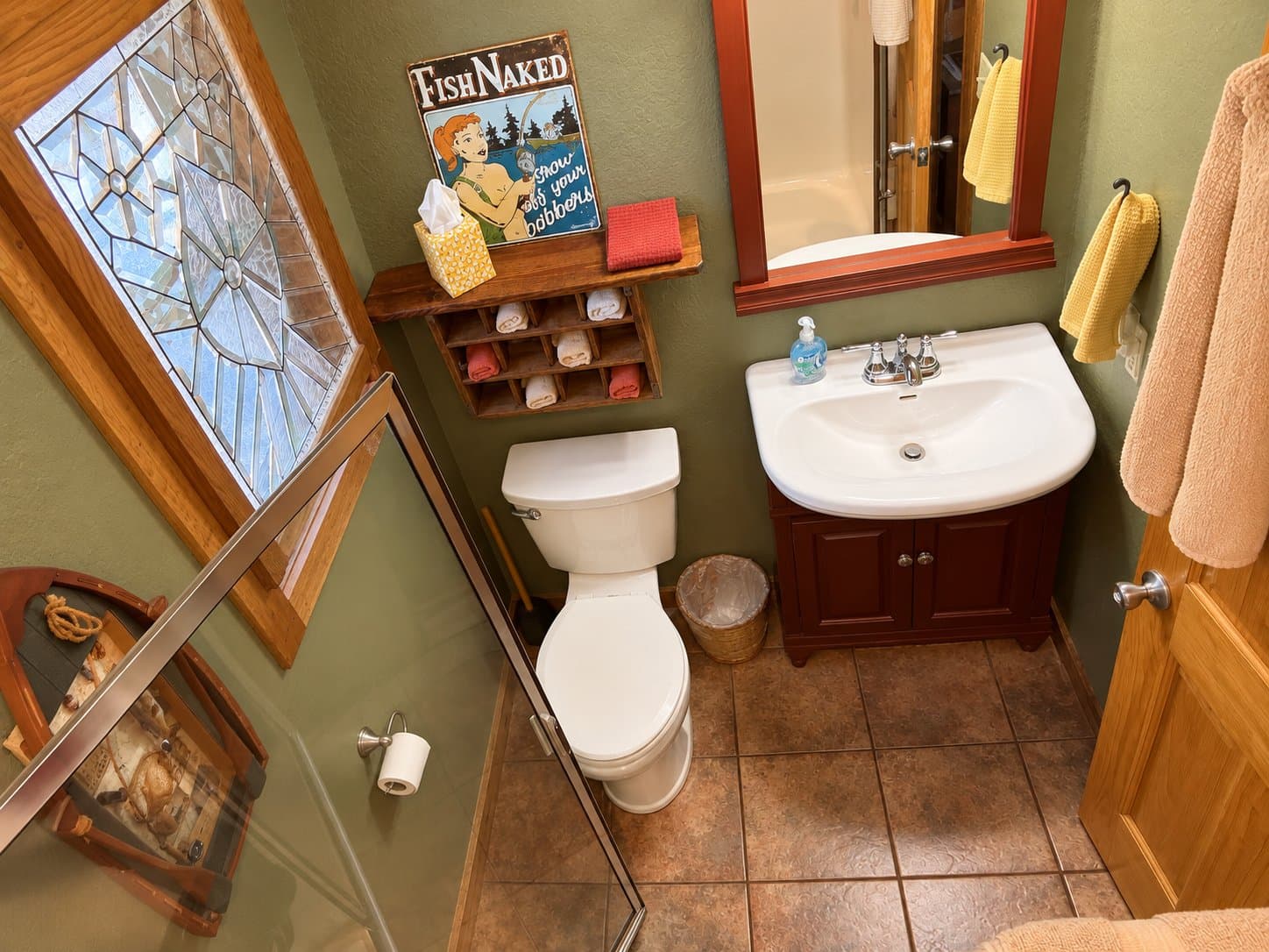 A small bathroom featuring a toilet, sink, decorative wall art, and a glass shower.