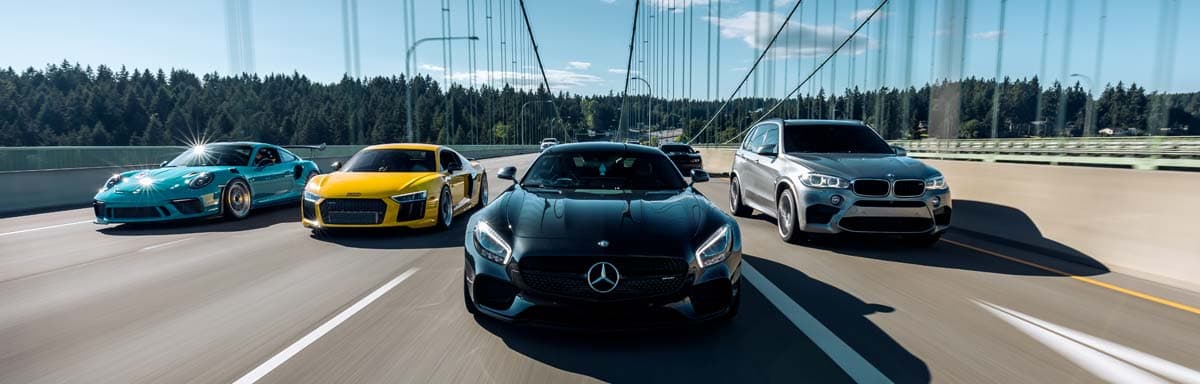 Five luxury cars driving on a bridge under a clear blue sky.