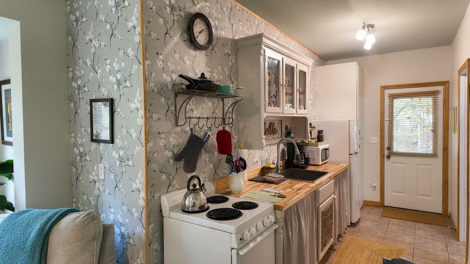 A cozy kitchen featuring floral wallpaper, a stove, and a door leading outside.