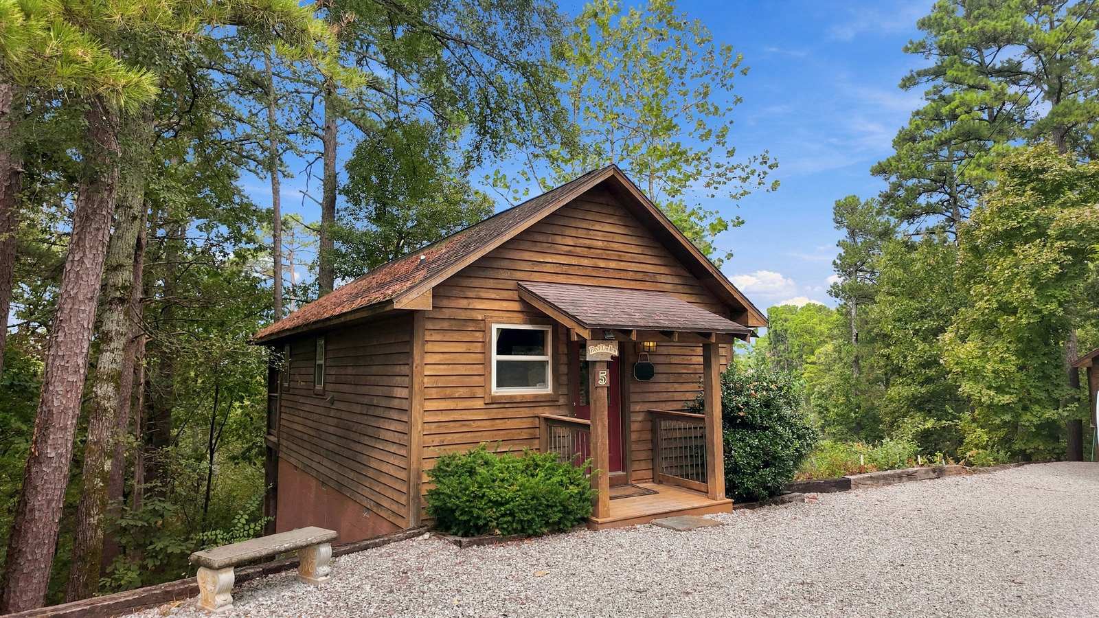 A small wooden cabin surrounded by trees and gravel driveway.