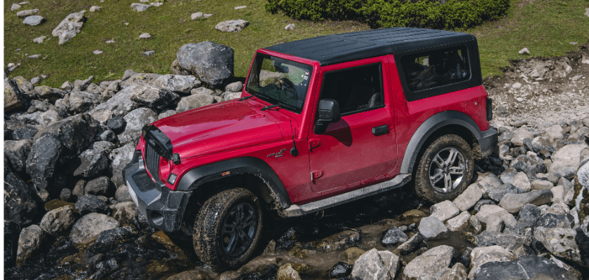A red off-road vehicle navigates rocky terrain near a stream. A red off-road vehicle navigates rocky terrain near a stream.