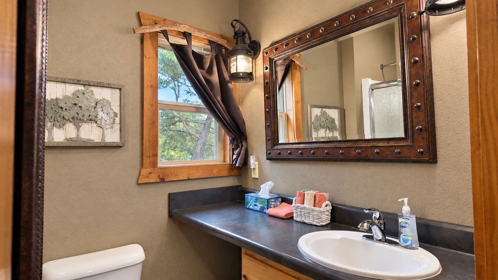 A cozy bathroom featuring a dark countertop, wooden accents, and a window with a view of trees.